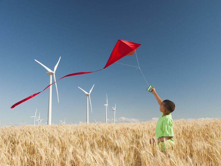 一个年轻的男孩用风力涡轮机飞过一个风筝。“class=