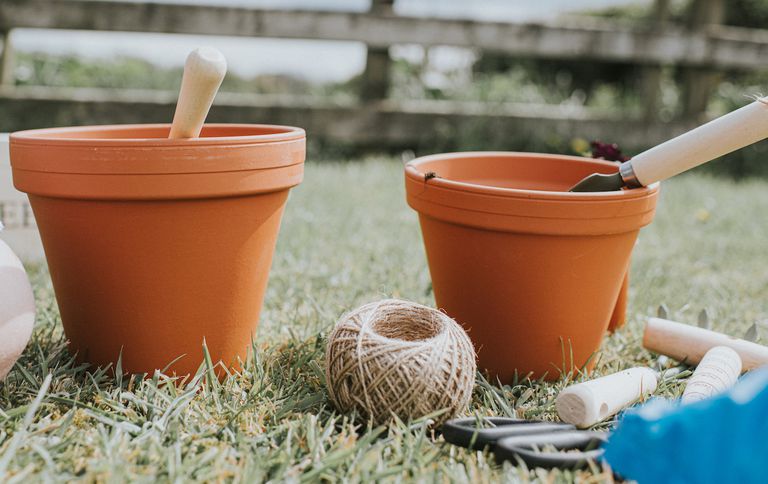 两个新鲜，新的，干净的赤土陶器罐在一个花园里，在篱笆前面。植物，绳子和前景中的各种其他园艺设备。