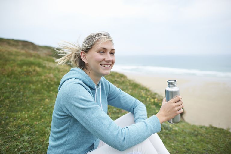 穿着运动服的女人坐在大西洋沿岸，手里拿着一个铝制水瓶