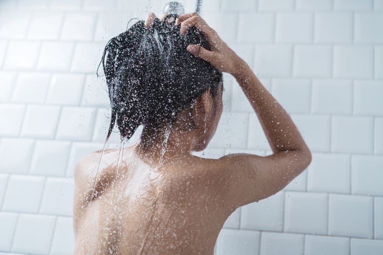 一位亚洲妇女在白色瓷砖浴室里用水洗头发。